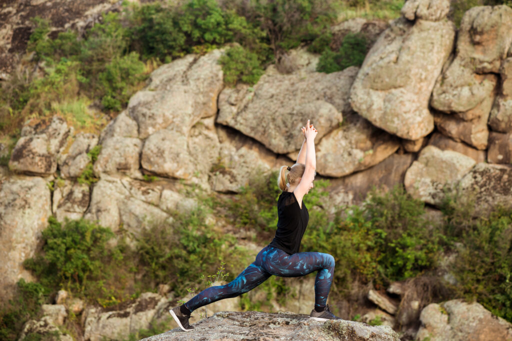 Beautiful blonde girl practicing yoga asanas on rock in canyon.
