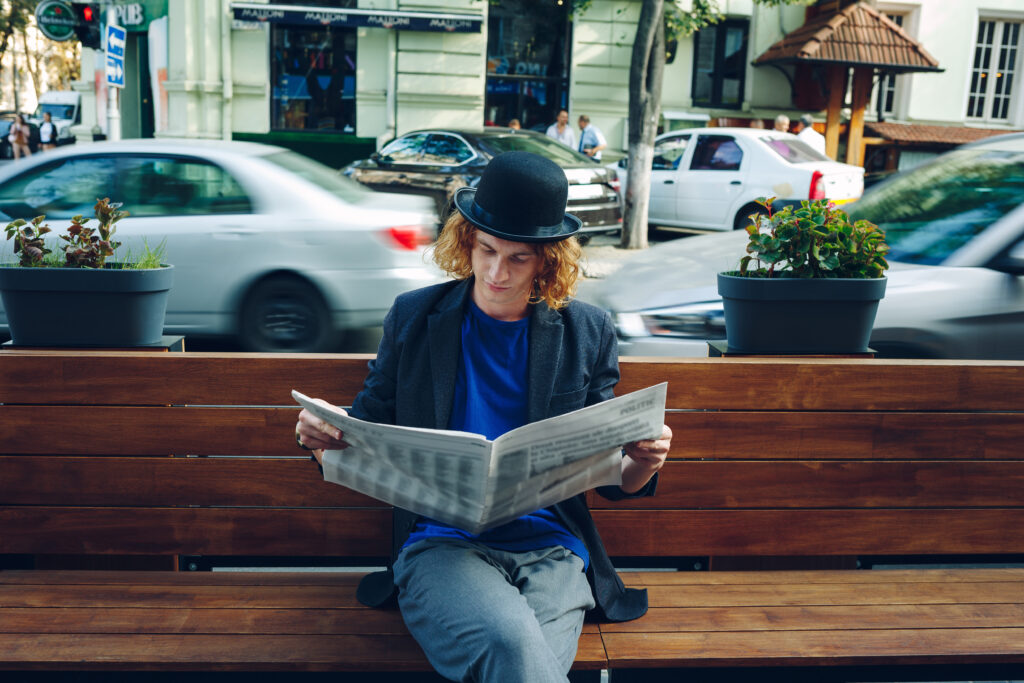 Red haired hipster man sitting on bench with newspaper