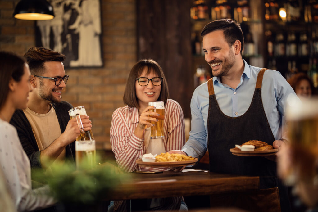 Happy waiter bringing food to group of people who are drinking b