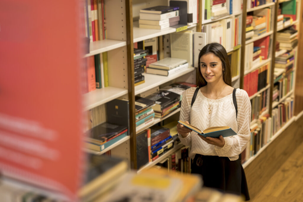 smiling-young-woman-with-book-near-bookshelf